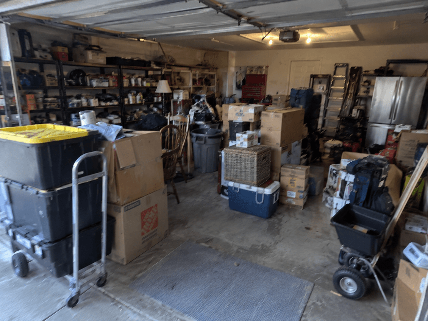 A garage crowded with boxes, bins, a cooler and full shelving
